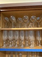 Shelf with seven wine glasses on top row and seven champagne flutes on bottom row.