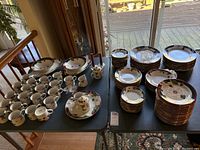Full view of china set on table, showing multiple stacks of dinner plates, salad plates, cups, serving bowls, and platters arranged with crystal items.