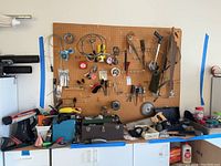 Wide shot of pegboard and workbench with assorted tools and hardware, including saw blades, hand tools, oil cans, and dispensers visible