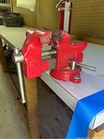Red Fuller bench vise mounted on the edge of a table, showing overall condition and size.