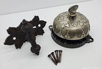 Overview of decorated domed door bell, cast iron knocker, and mounting screws on white background