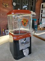 Front angled view showing black metal base, coin slot, and embossed glass globe with acorn decal.