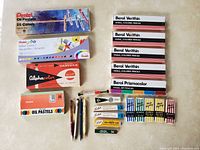 Photo showing boxes of Pentel oil pastels, Pentel watercolour paint set, Alpha-color pencils, Berol Prismacolor colored pencils, pens, and erasers