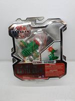 Two photos of sealed green Bakugan Gundalian Invaders Battle Gear Vilantor figures in clear plastic blister packaging with backing cards showing red and black branding and warnings.
