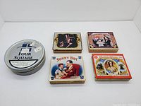 Five vintage cigarette and tobacco tins shown from top view, displaying branding and illustrations on lids