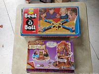 Photo showing two boxed games stacked; the top box is 1960's Beat the 8 Ball Game with vintage style art, below is Harry Potter Hogwarts Electronic Game box featuring kids playing and castle image.