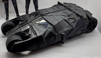 Top and side view of large black Batmobile action figure with detailed armor-like design and sturdy wheels.