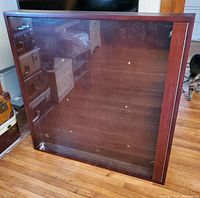 Front view of large wooden framed display case with glass front and locking key mechanism, standing upright on floor.