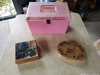 Pink 1950s plastic sewing box alongside two wooden decorative boxes on table