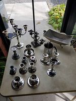 Entire lot of silver plate and pewter candle holders and candelabras on table outdoors near door, includes candelabras, candle holders, pewter dish, and silver plate mug.