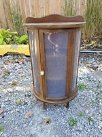 Front view of the small half-round wooden display case showing the curved clear plastic panel door with white knob and the curved top detail.