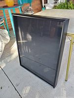 Angled front view of black-framed shadow box display with clear glass front and cloth backing visible.