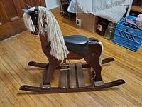Traditional dark wood children's rocking horse with black seat and yarn mane and tail.