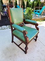 Three-quarter front view of chair showing carved wood frame and green vinyl upholstery