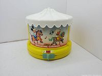Front and side view of the Disney Dreamtime Carousel music box showing colorful character illustrations on the carousel body with white canopy and yellow base.