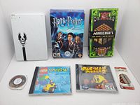 Top-down photo of the 7 items: Halo-themed hard drive, Harry Potter PC game, Minecraft card game, Lego Island PC game, Pac-Man World 2 PC game, Pac-Man keychain, 300 PSP UMD disc