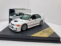 Front and side view of the white Mitsubishi Lancer EVO IV die-cast model car on black display base with gold nameplate.