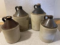 Four stoneware pottery crocks or jugs displayed together showing overall size and shape, with beige and brown coloring.