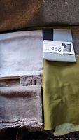 Photo showing linen fabric pieces in oatmeal, silver/blue, and dark grey colors alongside olive green leather piece.