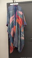 Full front view of the silk coverup showing multicolor abstract design with sweeping shapes in pink, orange and blue tones, hanging on hanger.