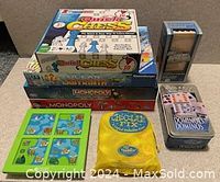 Boxed board games and accessories arranged on a floor including Quick Chess, Monopoly, Chocolate Fix, Dominoes, and miscellaneous game pieces.