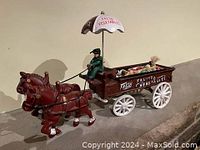 Full view of cast iron horse-drawn cart with driver and umbrella attached, showing the cart markings and wheels.