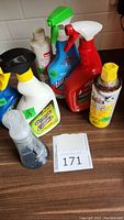 Seven open and used cleaning and maintenance products arranged on a counter, including Fantastik spray cleaner and Liquid Wrench can.