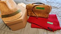 Photo shows natural straw sun hat with light green band, brown leather bowling bag with patented wear and broken handle, and red pleated fleece scarf with label visible.