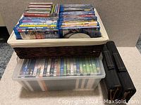 Wicker basket filled with children's DVDs on top of a clear plastic DVD bin with DVDs inside and two black DVD binders beside it.