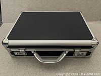Top view of the black hard shell briefcase showing silver trim, handle and two combination locks.