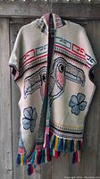 White hooded poncho with toucan and flower motifs and colorful fringe hanging outdoors