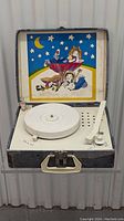 Full view of open vintage child's record player in case showing illustrated lid and player components.