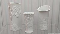Front view of the three white bisque porcelain vases with Art Nouveau/Art Deco style raised designs.