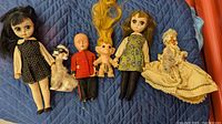 Photo showing six vintage dolls and figurines including two Susie Sad Eyes dolls, a RELCO Japan poodle figurine with sunglasses, a Sleepy Eyes soldier doll, a vintage troll doll, and a Victorian lady doll in cream dress.
