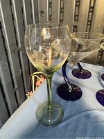 Green-stemmed wine glass with a clear bowl featuring etched floral designs beside three blue-stemmed martini glasses.