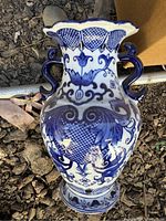 Close-up of one blue and white porcelain vase showing detailed chinoiserie blue patterns and double handles with scalloped rim.