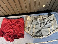 Two pairs of shorts shown side by side on a blue surface, left red athletic shorts, right distressed denim shorts.