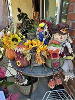 Wide view of all fall decorations including two scarecrow figures on pumpkin bases, decorative bird, sunflower bouquet, and wreath on a porch table.