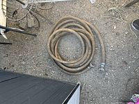 Top-down view of a coiled brown fire hose on the ground with metal connectors attached.