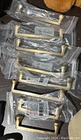 Six large gold drawer pull handles individually packaged in clear plastic bags.