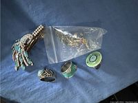 Lot of green jewelry including peacock brooch, rings, and necklace on blue fabric