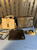 Four purses including beige, bronze Anne Klein, black Kangaroo Coin, and small fur accessory laid out on blue fabric
