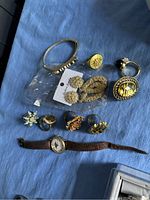 Full view of lot showing various pieces of golden costume jewelry and the watch on blue fabric background.