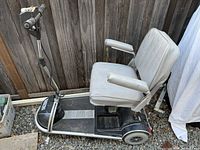 Full side view of the mobility scooter showing padded armrests, cushioned seat, and base with wheels on gravel surface.
