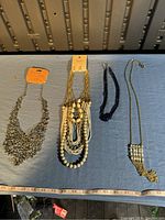 Four assorted necklaces laid out on a surface, showing a variety of styles including chain, beaded, and multi-strand designs.