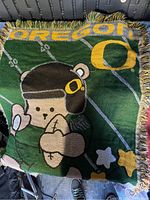 Photo showing folded green baby blanket with Oregon football mascot and the word 'OREGON' in yellow letters, with fringed edges.