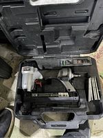 Single image showing the 18 gauge pneumatic stapler inside a black molded plastic carrying case, accompanied by bundles of metal staples and a small accessory or tool.