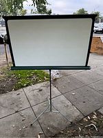 Front view of vintage folding projection screen set up outdoors on tripod stand.