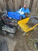 Toy trucks including a yellow dump truck, blue airplane truck, and gray monster truck toy outside with dirt and wear