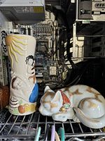 Photo showing the ceramic vase illustrated with a sun and a woman holding a blue vase, next to a sleeping cat ceramic figurine.